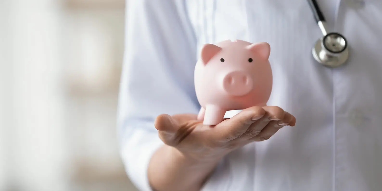 Doctor holding a pink piggy bank in an open hand, symbolizing healthcare savings.