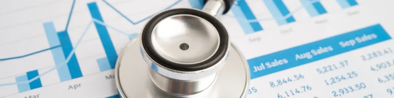 Stethoscope resting on printed sales charts and financial graphs.