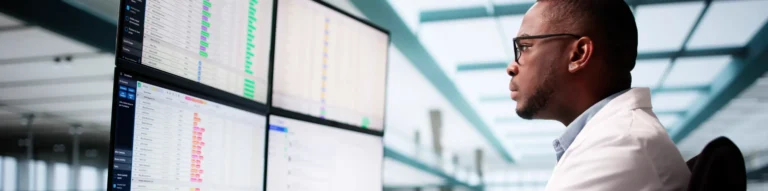 Healthcare data analytics professional reviewing operational dashboards across multiple monitors